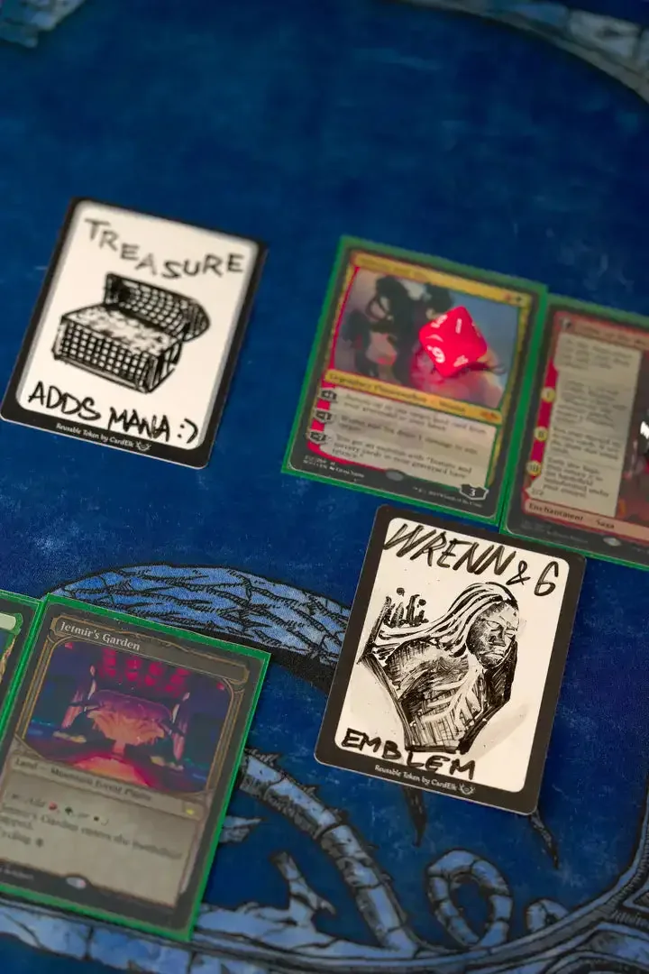 A hand-drawn Wrenn and Six emblem on a CardElk reusable token, next to a treasure token on a blue playmat